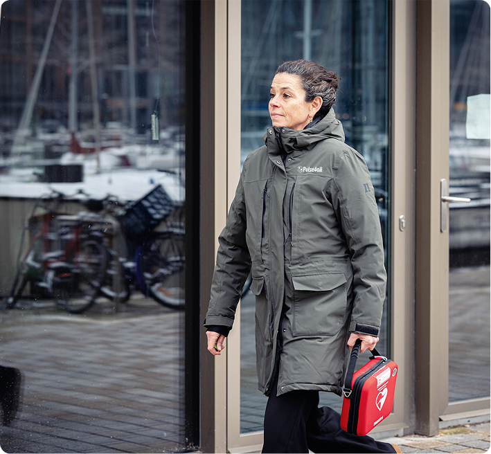 Vrouw in Pulse4all-jas draagt een Philips AED in een rode koffer over straat