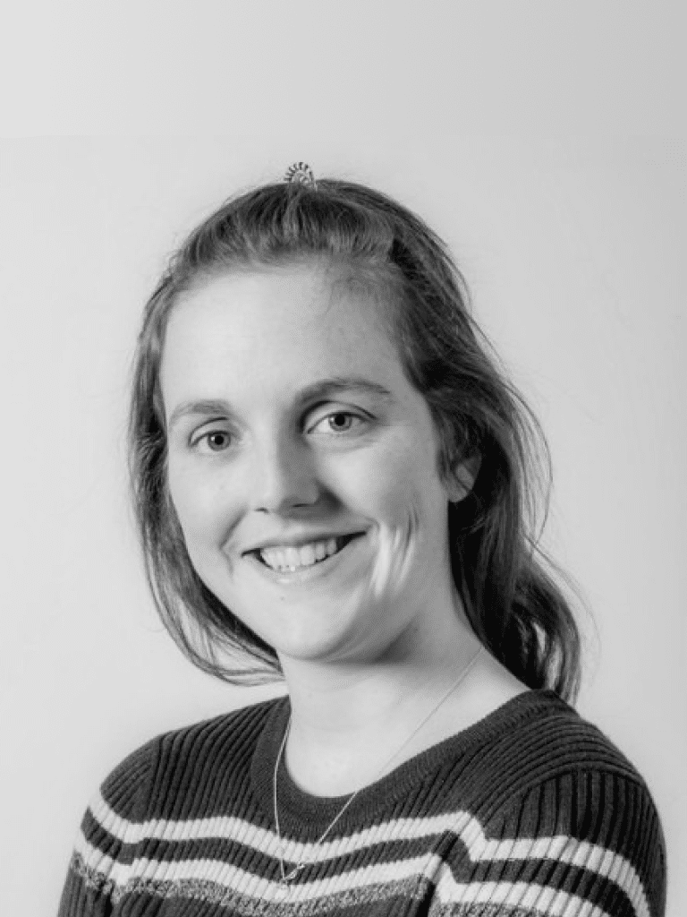 Jonge vrouw in een gestreept truitje lacht terwijl ze poseert tegen een lichte muur.